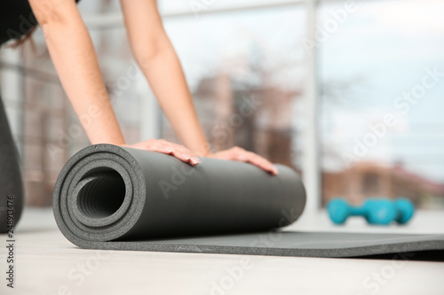Woman rolling yoga mat on floor indoors, closeup