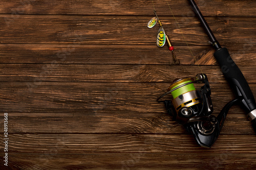 Spinning with a reel on an old brown wooden background. Metal Fishing lure. Beautiful relief boards. Carbon rod. Fishing. Summer. Place for text.