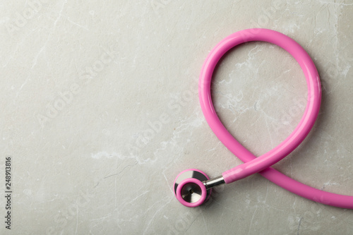 Pink stethoscope folded like awareness ribbon on grey background, top view with space for text. Breast cancer concept