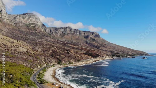 Aerial view of the beach and Twelve Apostles range in the background. Popular tourist and hiking location. Amazing blue ocean and beautiful seascape. Cars driving on the coast road. Drone backing.