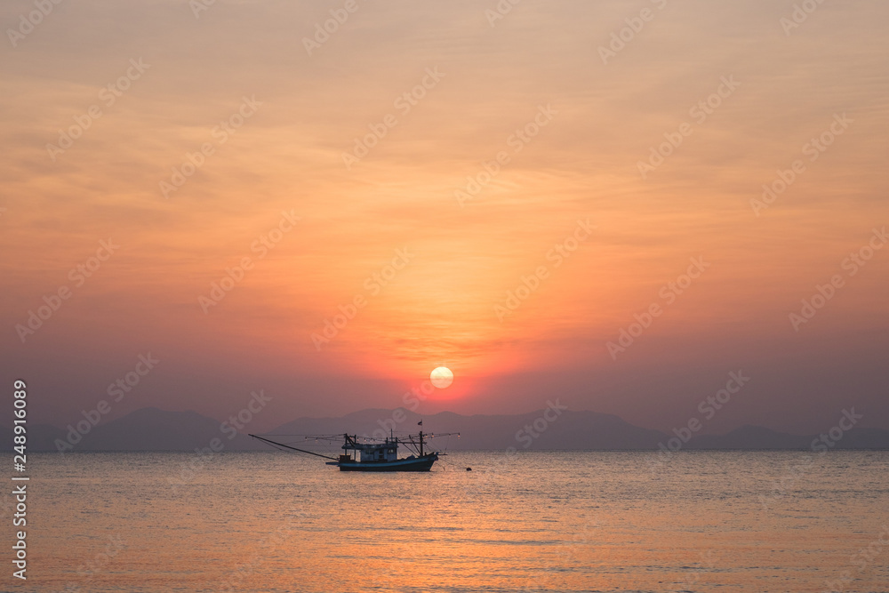 Lonely fishing boat in the sea at sunset with a silhouette of mountains on the horizon