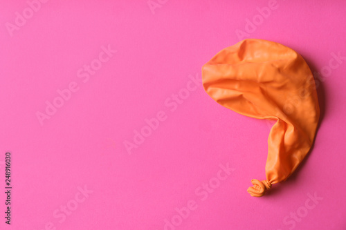 Orange deflated balloon on color background, top view with space for text photo