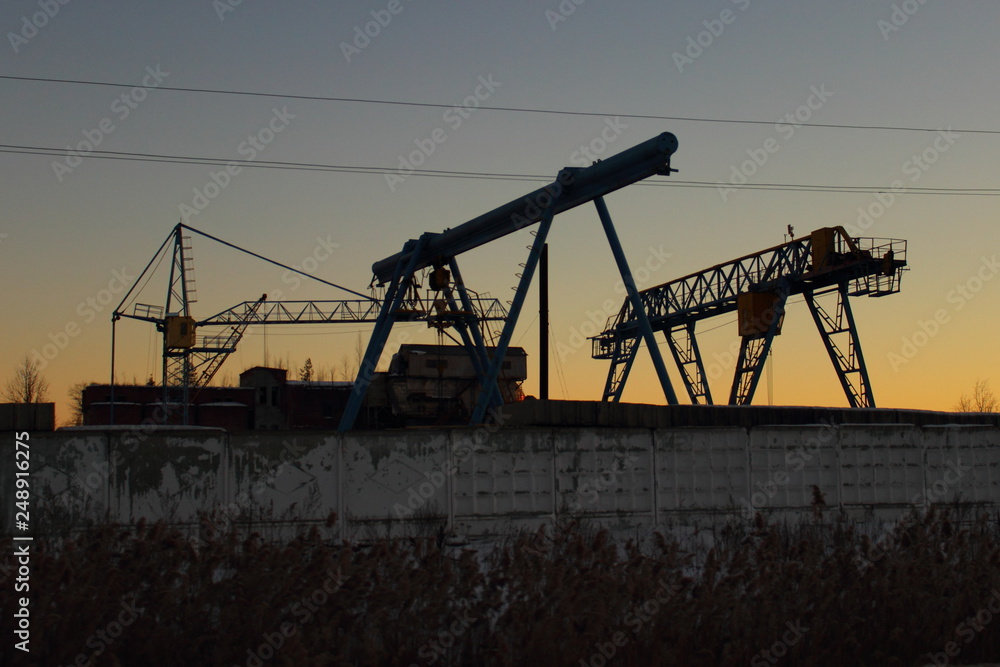 Smolensk / Russia - industrial landscape, silhouette portal cranes in dusk behind a concrete fence in winter, ecology, environment