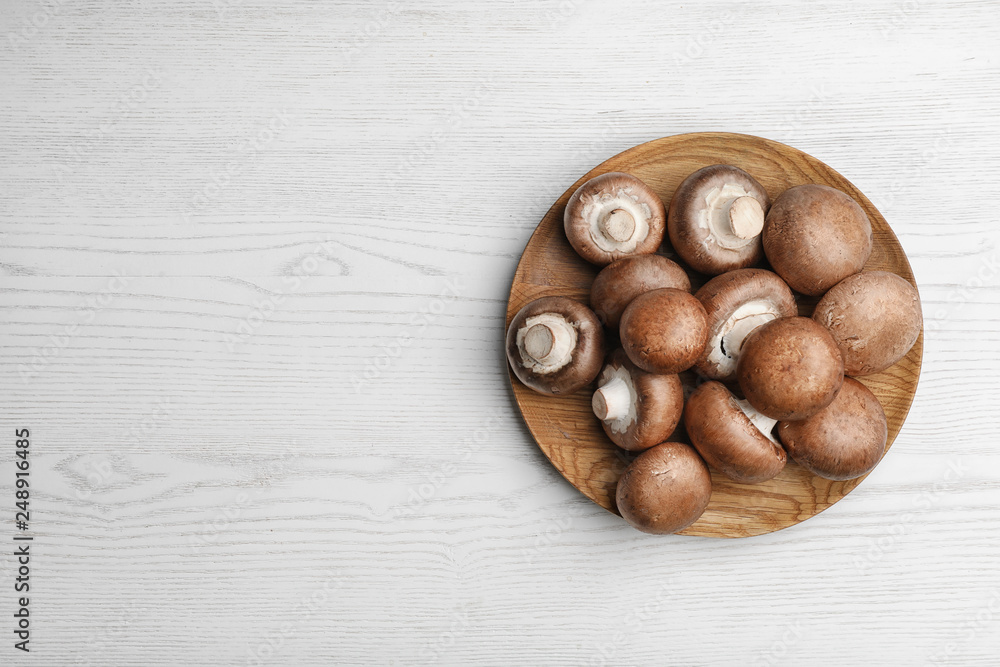 Obraz premium Plate with fresh champignon mushrooms on wooden table, top view. Space for text