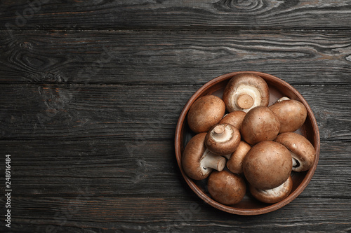 Bowl with fresh champignon mushrooms on wooden table, top view. Space for text