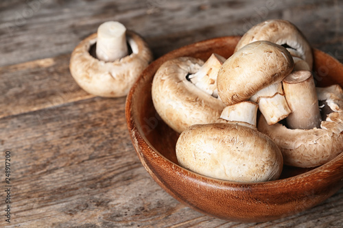 Bowl of fresh champignon mushrooms on wooden table, closeup. Space for text