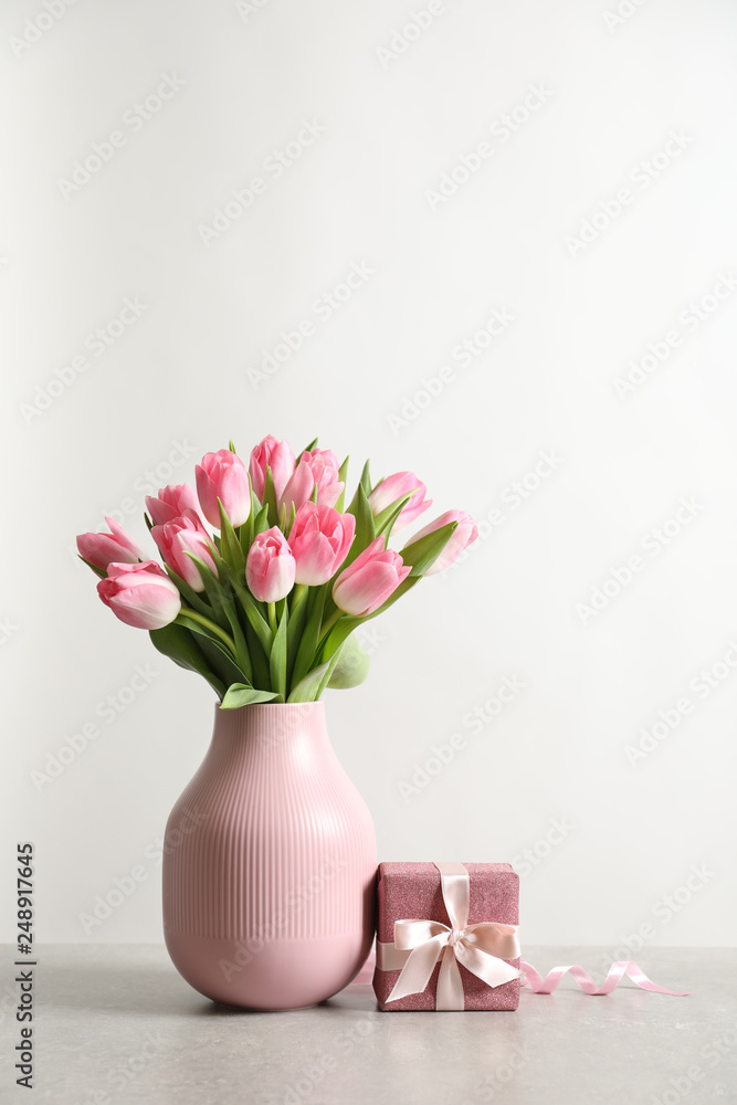 Obraz premium Bouquet of beautiful spring tulips in vase and gift box on table against white background. International Women's Day