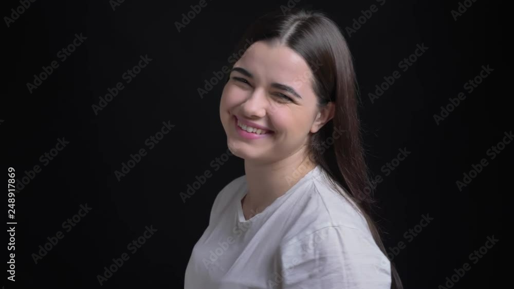Portrait of young overweight brunette caucasian girl turns to camera and watches smilingly into camera on black background. Portrait of young overweight brunette caucasian girl turns to camera and watches smilingly into camera on black background.