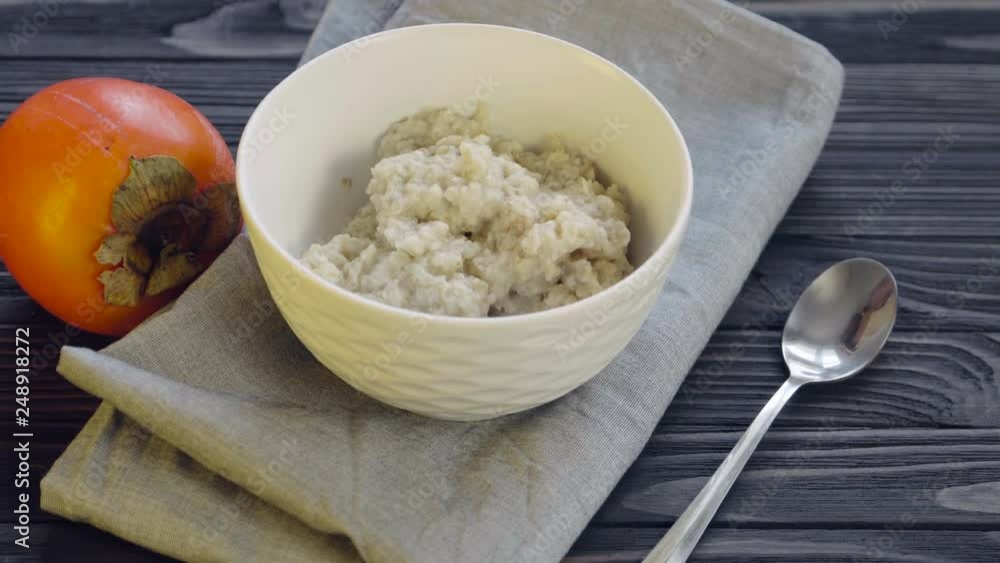 Healthy food. Oatmeal in a deep bowl top view. Cooking healthy breakfast- oatmeal with persimmon. Slow panning from bottom to top