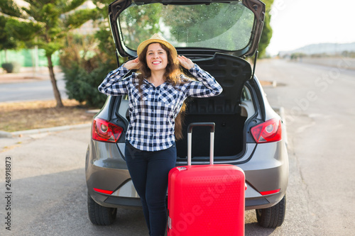 Happiness, travelling and people concept - young woman standing near back of car smiling and getting ready to go. Summer road trip