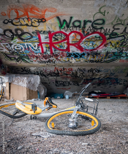 Old yellow scrap bicycles under concrete stairs with graffiti and homeless sleeping shelter