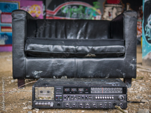 Black leather armchair and old radio in a chilled creative shelter under a bridge with graffitis in background