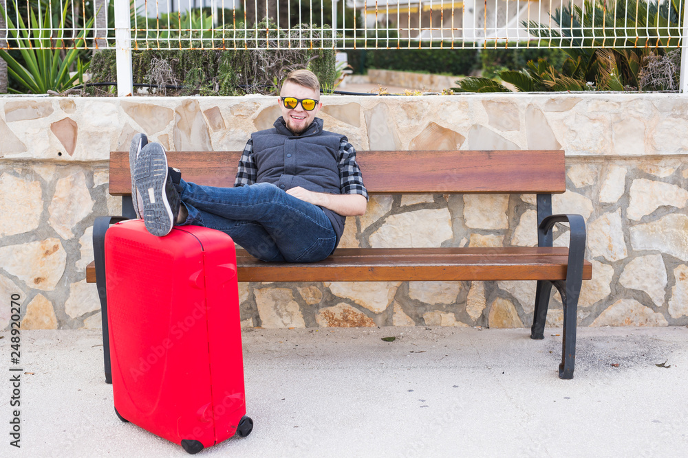 Travelling, people and holiday concept - young man sitting with suitcase. He is ready to trip