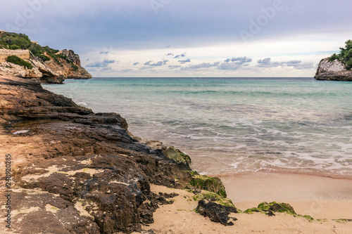 Wellen brechen sich weiß schäumend am sandig, felsigen Strand auf Mallorca