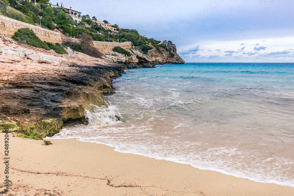 Wellen brechen sich weiß schäumend am sandig, felsigen Strand auf Mallorca