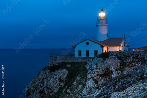 Leuchtturm auf einem Felsen umringt vom Meer, zur blauen Stunde