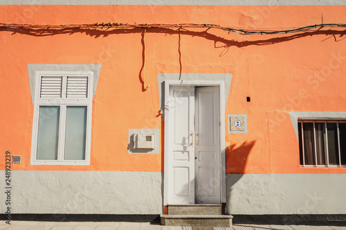 A facade of a vibrant orange house with a window and an open white front door in Galdar, Gran Canaria