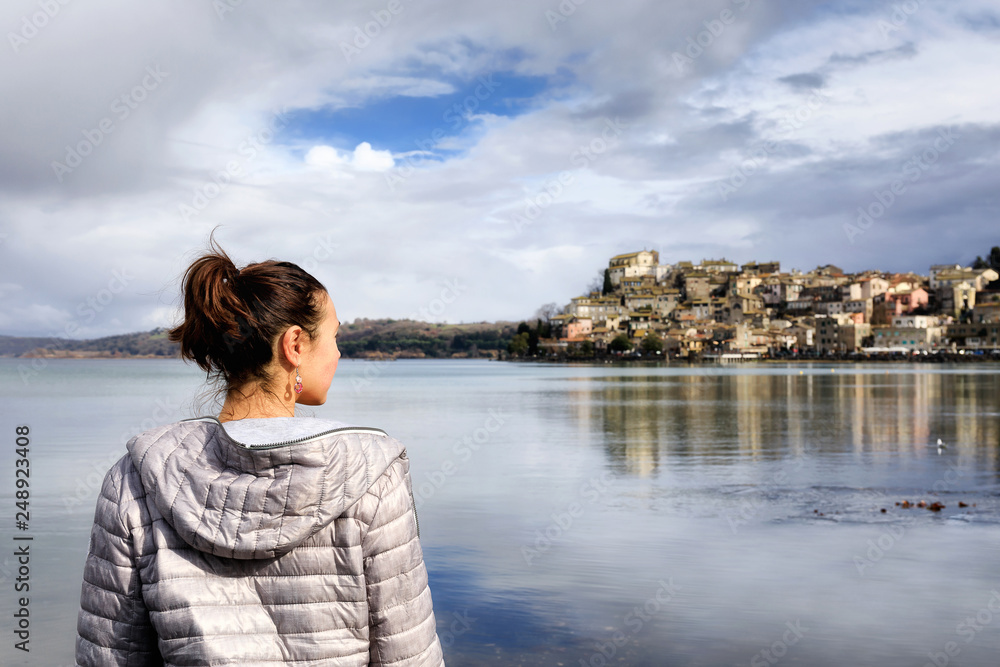 Girl at the lake and small village in the distance. Girl on the shore of the lake looks at the horizon in the distance, the houses of the village overlooking the water. On a winter morning at Lake Bra