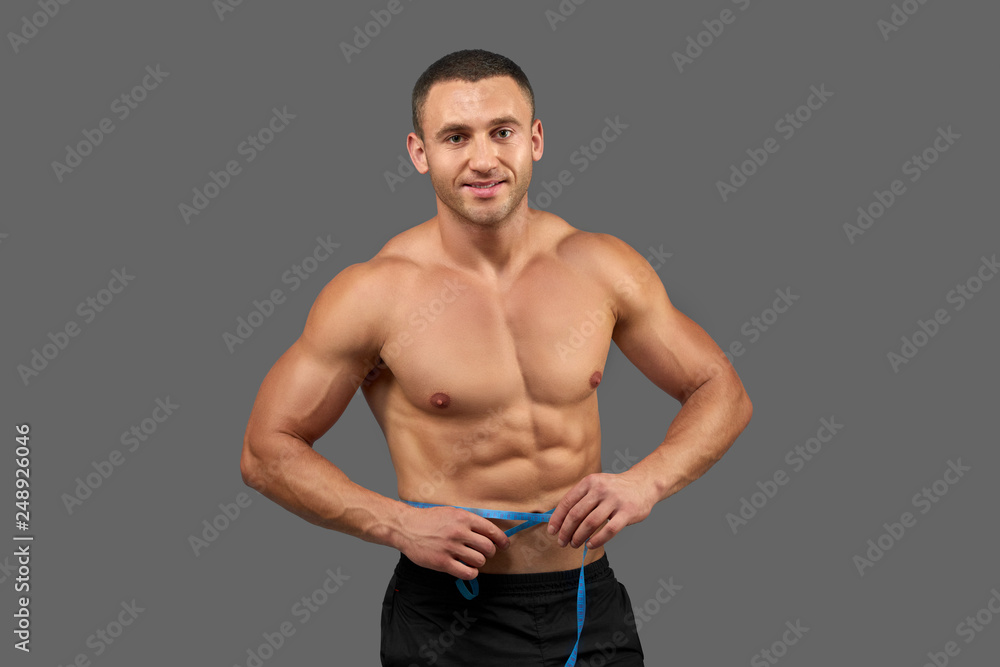 Fototapeta premium Sexy bodybuilder holding measure tape round waist.