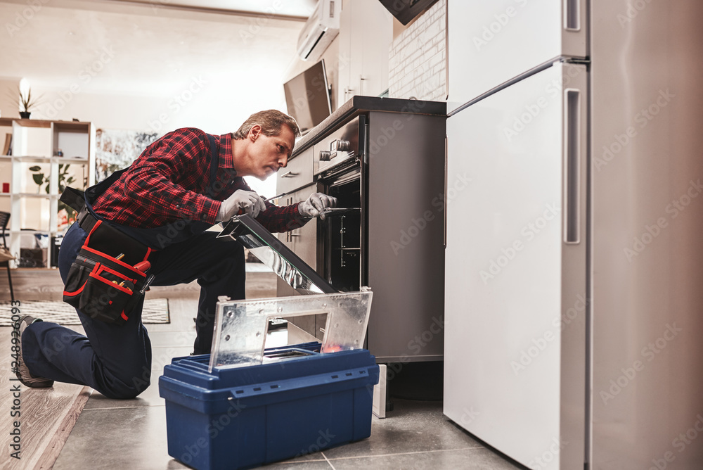 Whats up with oven. Full length of repairman examining oven Whats up with oven. Full length of repairman examining oven