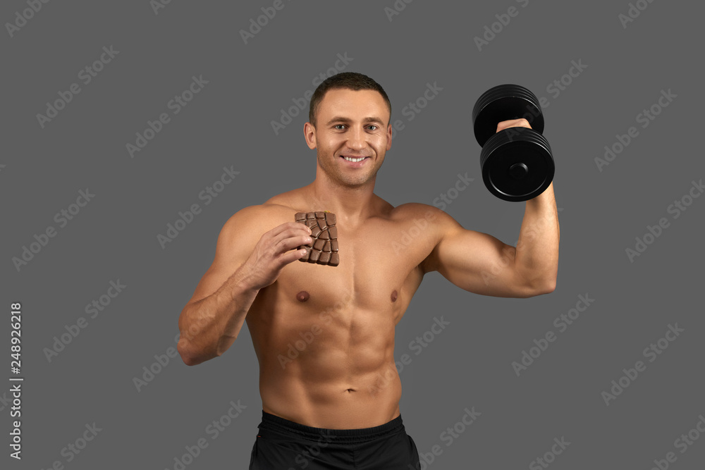 Bodybuilder holding dumbbell and chocolate bar.