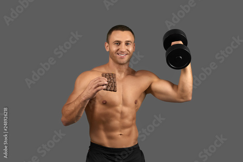 Bodybuilder holding dumbbell and chocolate bar. © serhiibobyk