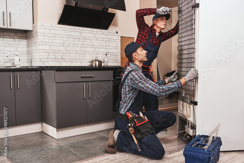 Two handymen with refrigerator. Young men mechanics checking refrigerator photo