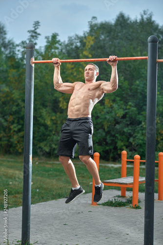 Sportsman working out outdoors, doing pull ups.