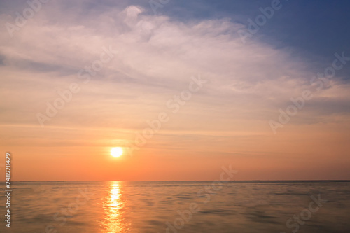 Colorful sunset and sea background with blue  purple and orange tones in abstract idea. It is small orange sun in sky at twilight time and copy space.