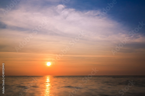 Colorful sunset and sea background with blue, purple and orange tones in abstract idea. It is small orange sun in sky at twilight time and copy space.