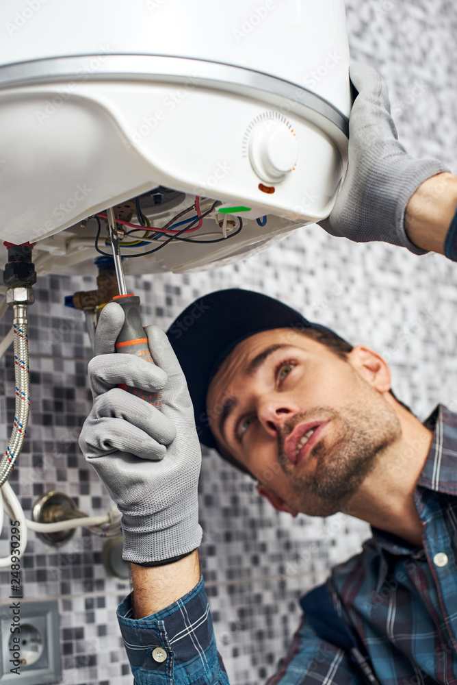 Fototapeta premium Set up boiler. Worker set up electric heating boiler at home bathroom
