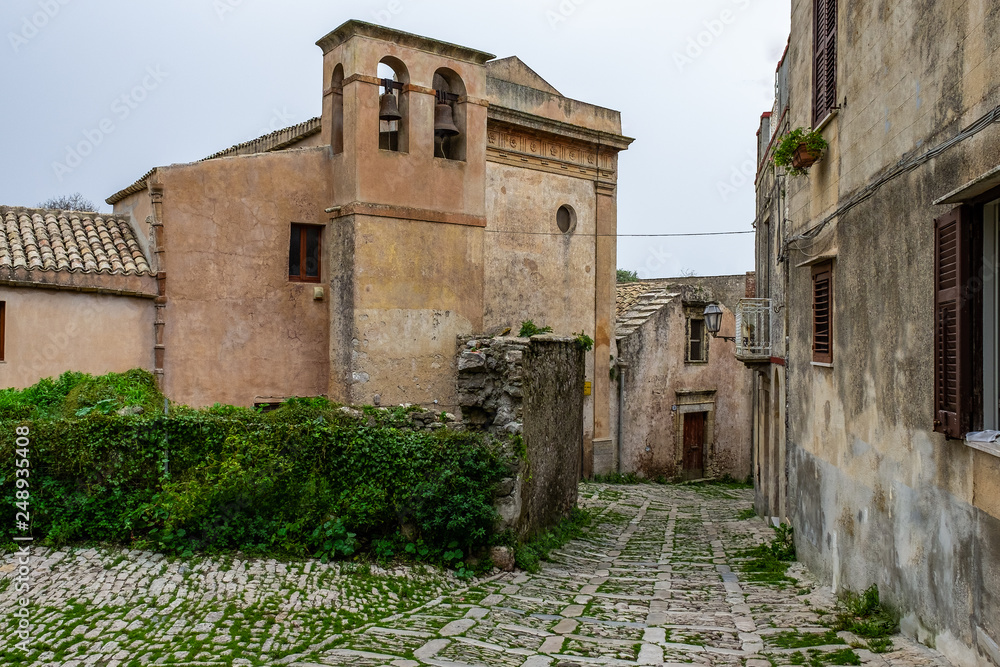 Typical narrow stone street in the medieval historical center of Erice with the church tower in background, Sicily