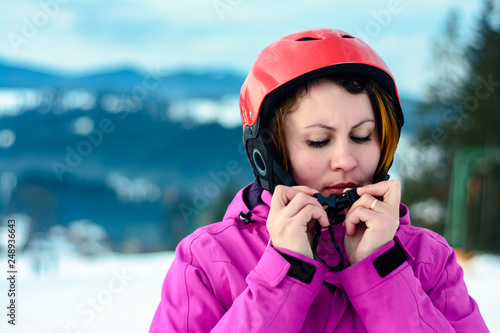 A beautiful woman skier wears a helmet and fixes it for safety