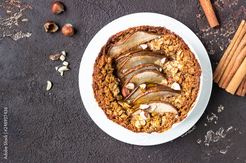 Diet crumble with oatmeal, cinnamon and pears decorated with hazelnut and honey in a frying pan for baking. Dark brown stone concrete. Top view, copy space.