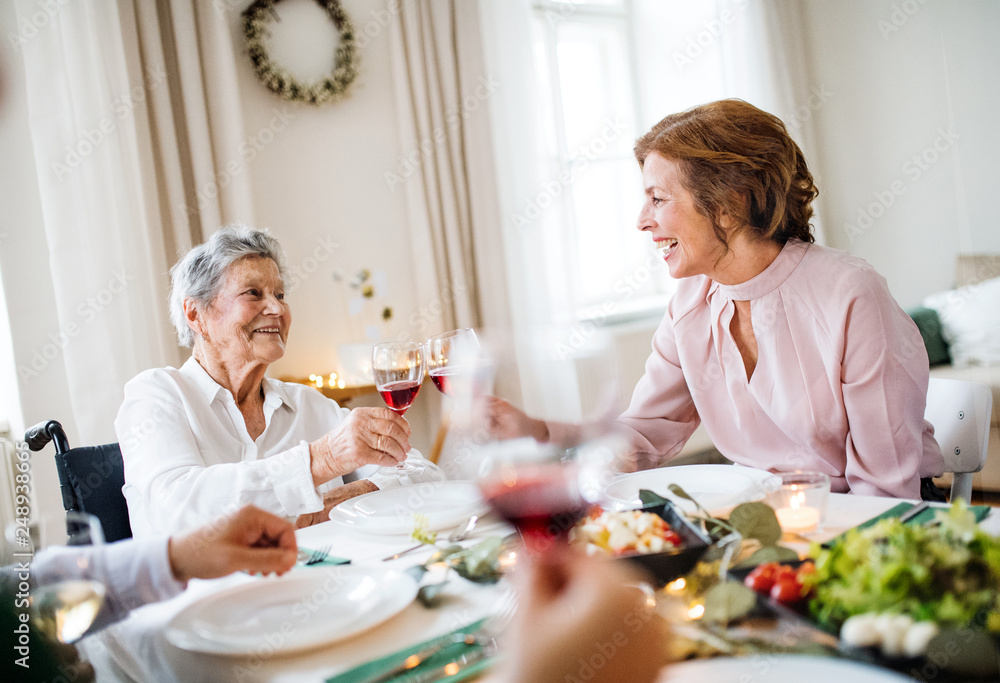 An elderly woman in wheelchair sitting at the table on a indoor party, clinking glasses.