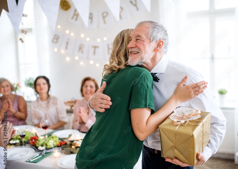 Young woman giving a gift to her grandfather on indoor party, hugging