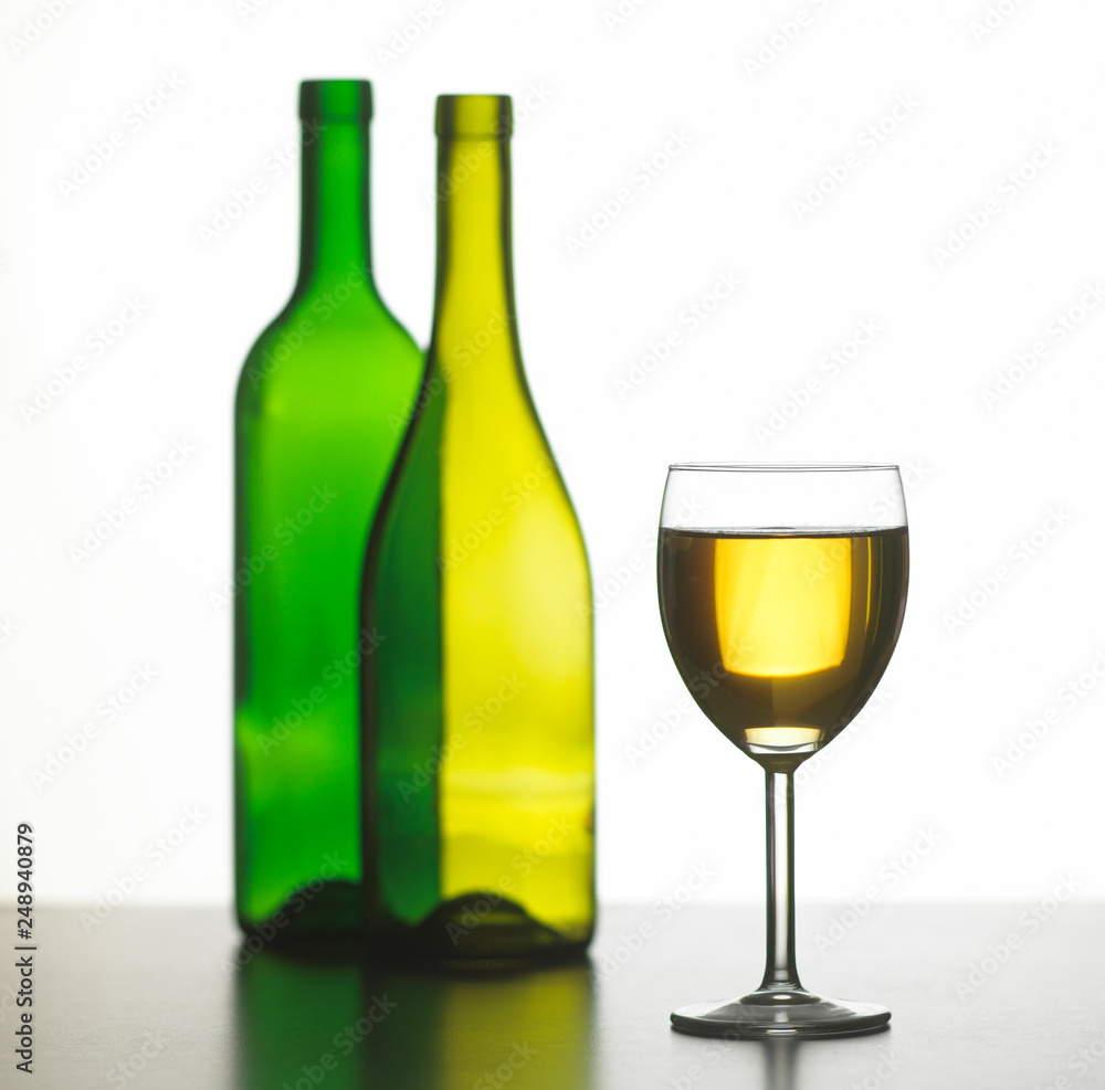 GLASS OF WHITE WINE WITH TWO GREEN WINE BOTTLES ON WHITE BACKGROUND GLASS OF WHITE WINE WITH TWO GREEN WINE BOTTLES ON WHITE BACKGROUND