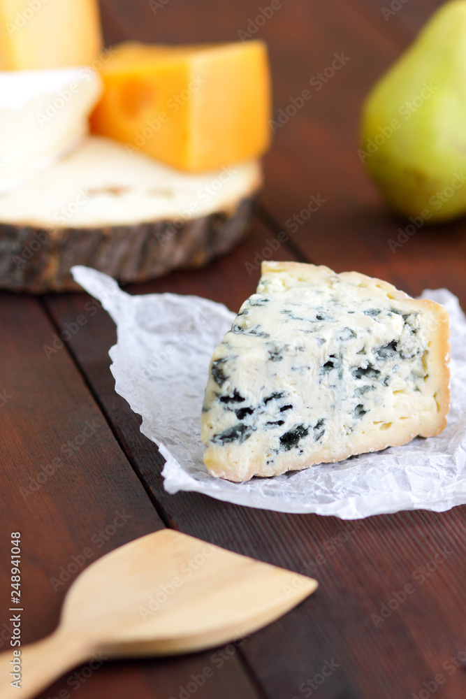 Various types of cheese and pear on wooden boards. Slices of cheese on blurred background. Dorblu, camembert and hard yellow cheese on parchment paper