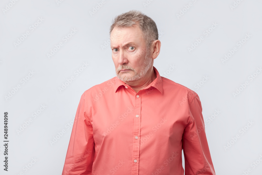 Fototapeta premium Senior man in red shirt frowning and squinting, showing disbelief or doubt