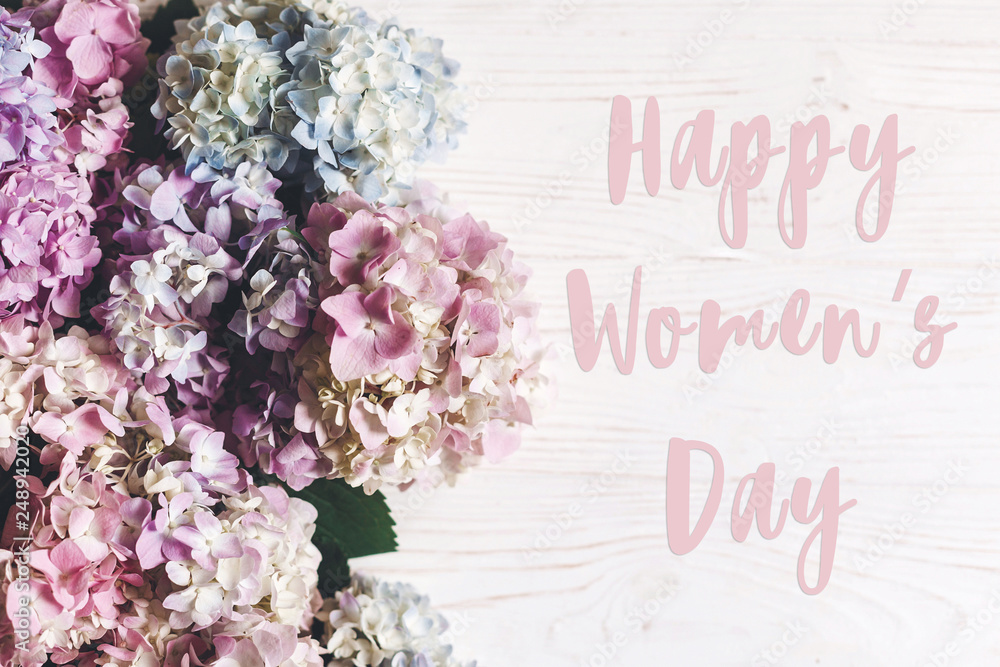 Happy Women's Day text sign on beautiful hydrangea flowers on rustic white wood, flat lay. Colorful border of hydrangea. Stylish floral greeting card. International womens day 8 march Happy Women's Day text sign on beautiful hydrangea flowers on rustic white wood, flat lay. Colorful border of hydrangea. Stylish floral greeting card. International womens day 8 march