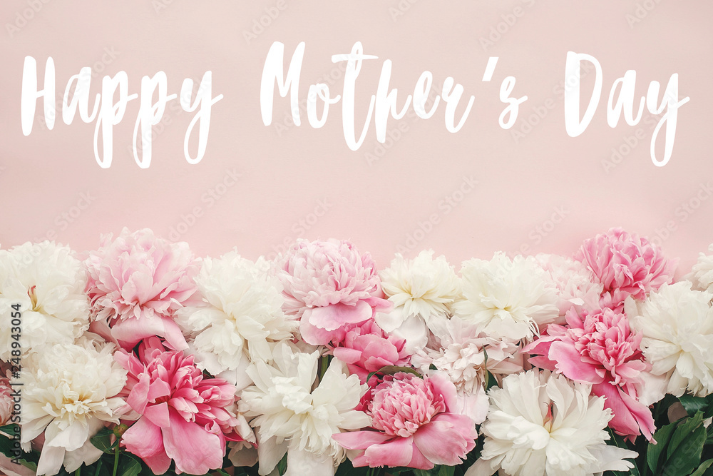 Happy Mother's Day text sign on peonies flat lay. Pink and white peonies border on pastel pink paper with space for text. Stylish floral greeting card. Happy Mother's Day text sign on peonies flat lay. Pink and white peonies border on pastel pink paper with space for text. Stylish floral greeting card.