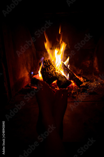 Bare legs of young woman are heated by open fire in fireplace