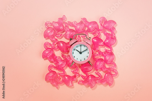 Alarm clock and pink flamingo toys on pastel pink coral background. Flamingo time for rest and relax. Creative layout concept gift party for birthday. Minimal summer concept with copy space, flat lay
