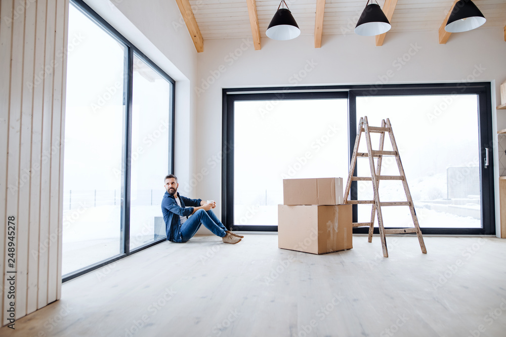 A mature man with cardboard boxes sitting on the floor, furnishing new house.