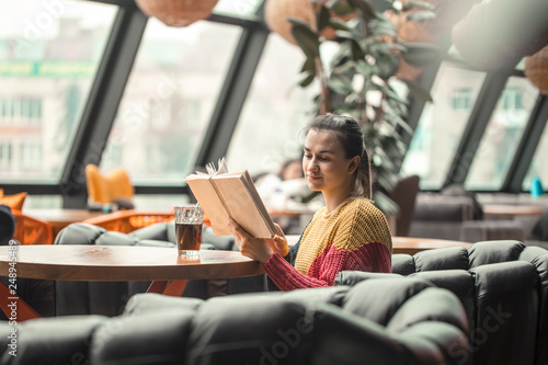 Young beautiful woman in orange sweater reading interesting book in cafe © puhimec