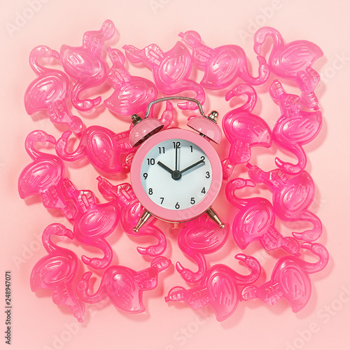 Alarm clock and pink flamingo toys on pastel pink coral background. Flamingo time for rest and relax. Creative layout concept gift party for birthday. Minimal summer concept with copy space, flat lay