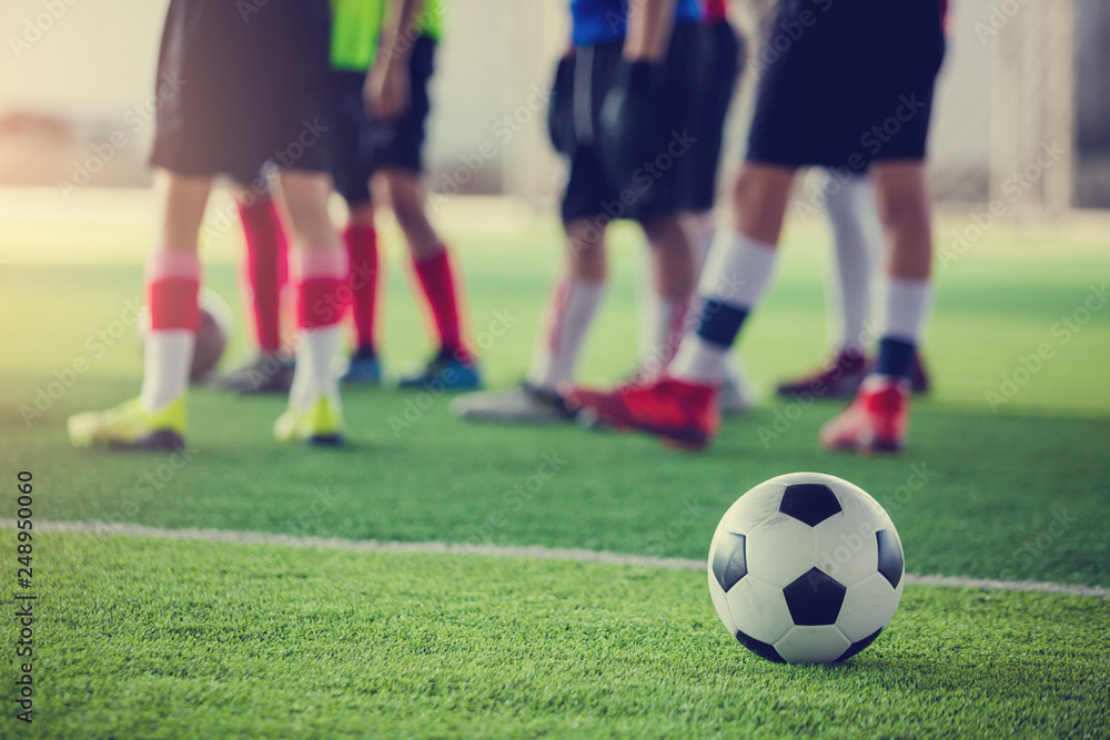 soccer ball on green artificial turf with blurry soccer players standing