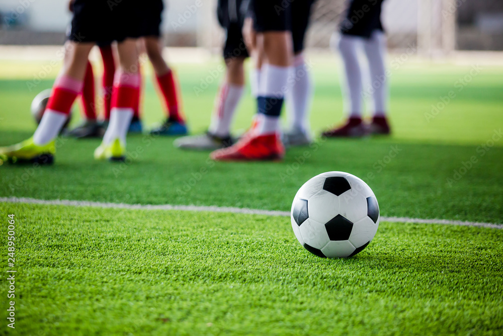 soccer ball on green artificial turf with blurry soccer players standing