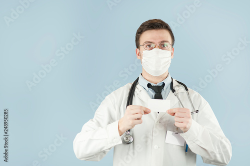 Doctor holding copy space. Close-up of a confident young doctor showing his business card and smiling while standing against blue background