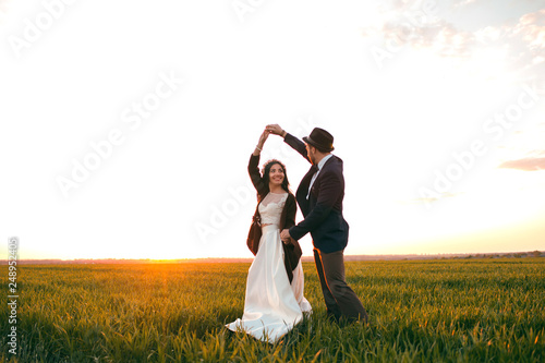 Groom holding bride in dance pose on wedding dayThe groom holds the bride in a dance pose on the wedding day, a young couple dancing at sunset, a stylish groom and a beautiful bride photo